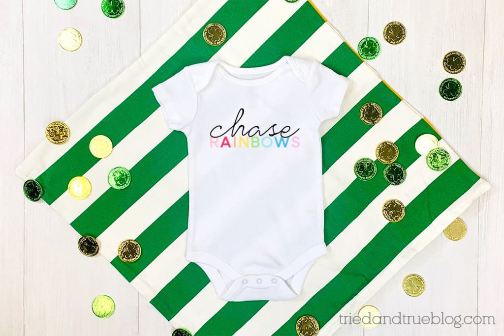 White baby onesie on green/white striped background with the words 