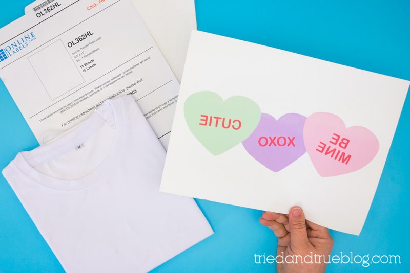 Hand holding iron-on transfer paper with the reversed image of conversation hearts.