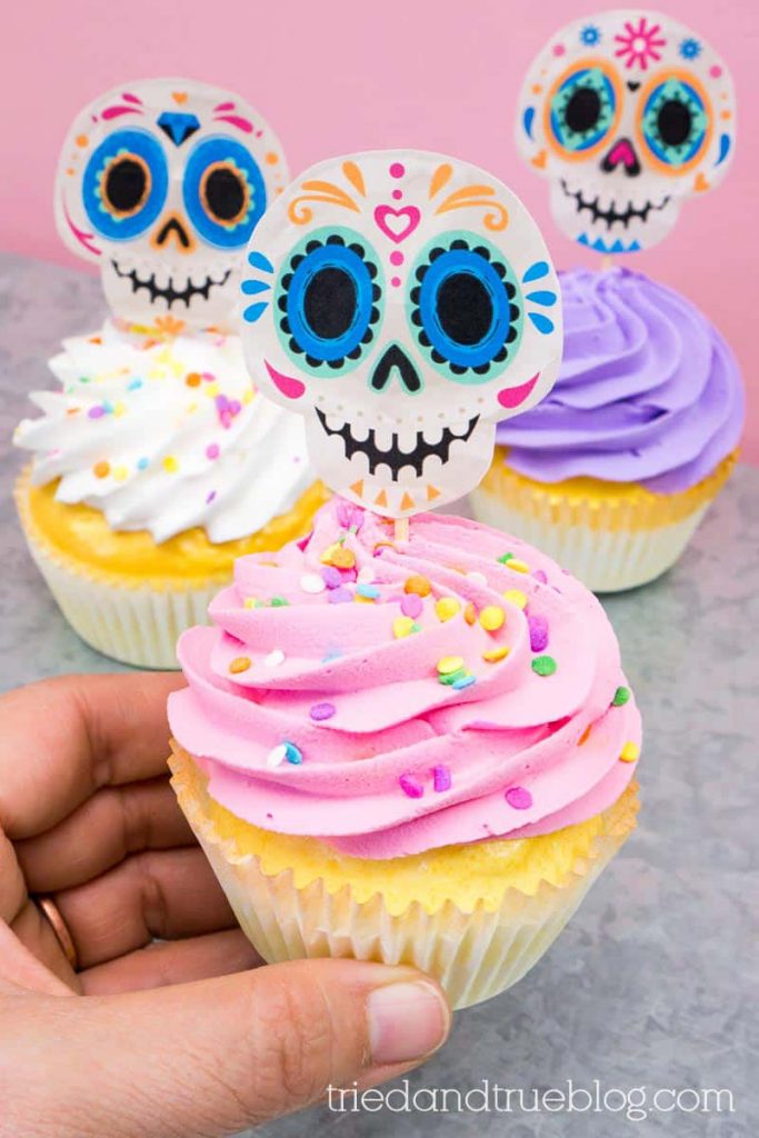 Hand holding pink frosted cupcake with Day of the Dead (Dia de los Muertos) Sugar Skull Cupcake Topper.