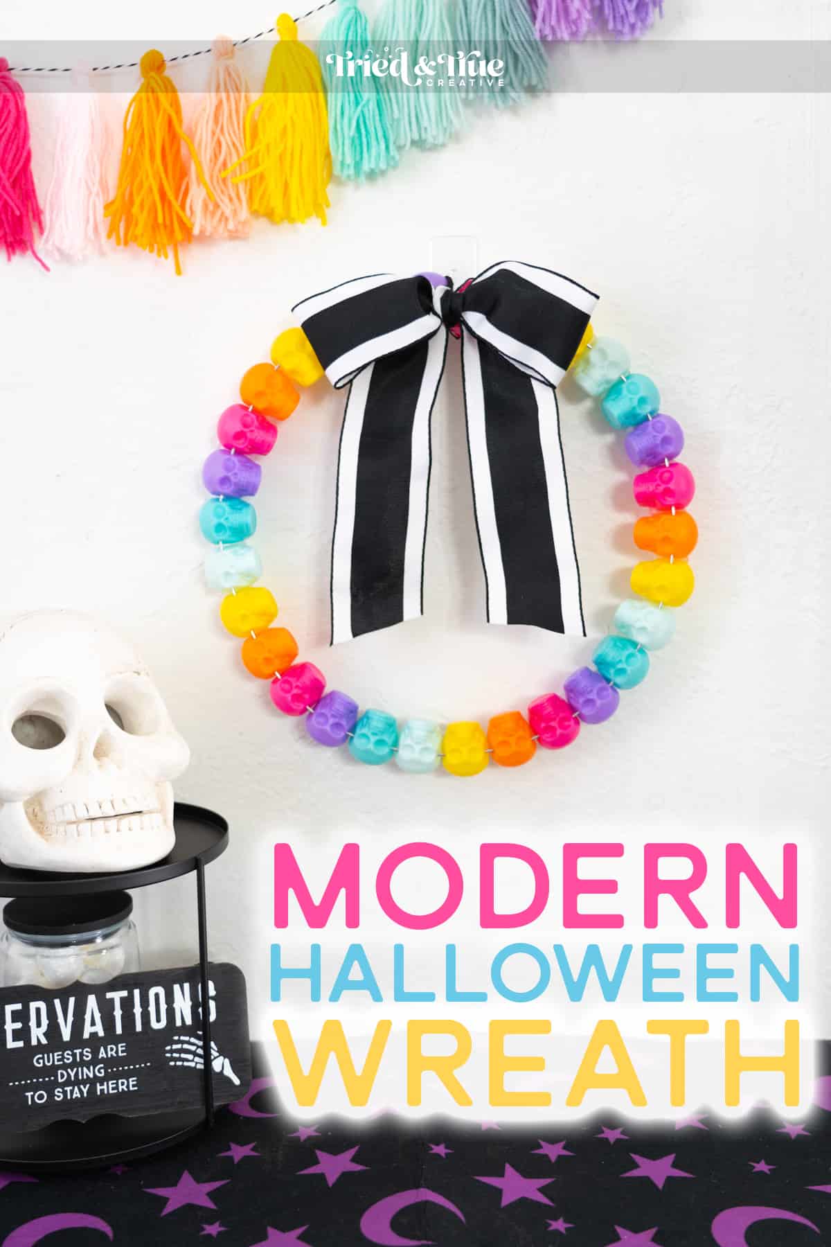 Colorful Halloween Wreath craft made of colorful skulls on a white wall with Halloween decor surrounding it.