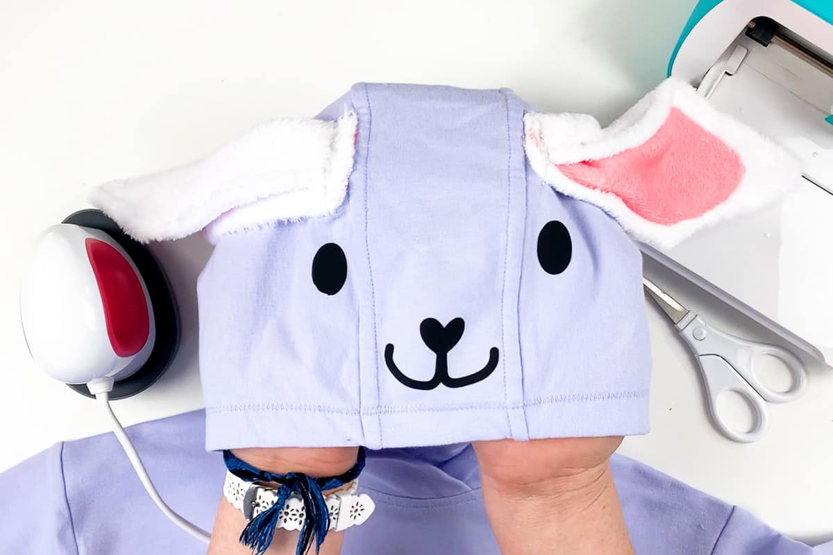 Hand holding purple sweatshirt hoodie with white bunny ears and black face. (Easter Bunny Hoodie)