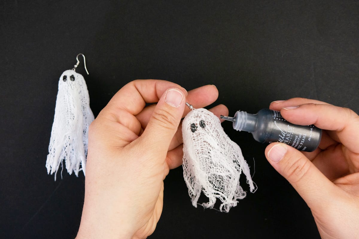 Hands adding black eyes with paint to cheesecloth ghosts.
