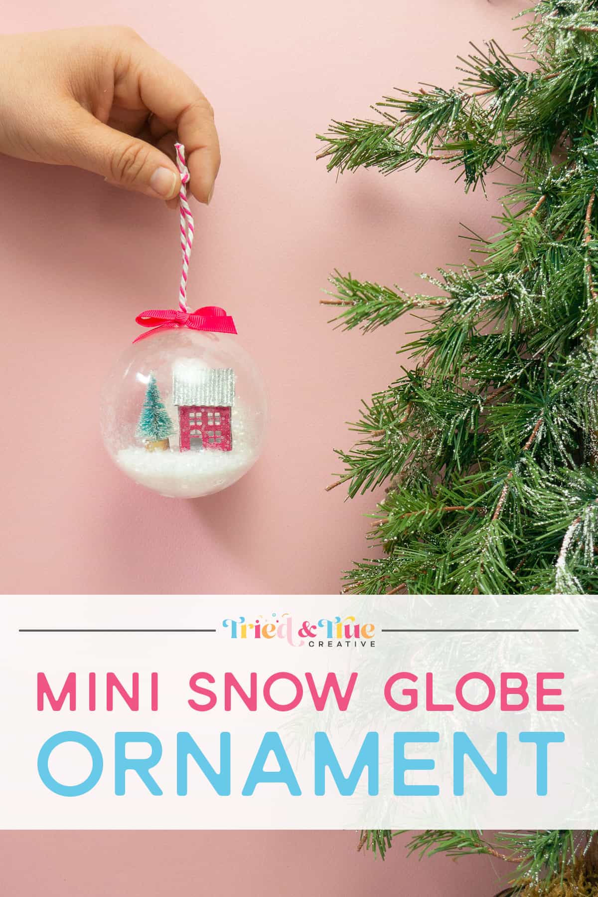 Hand holding a mini snow globe ornament next to greenery with words.