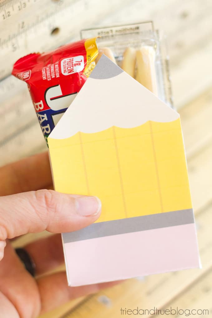 Hand holding a printed gift box in the shape of a pencil with snacks inside.