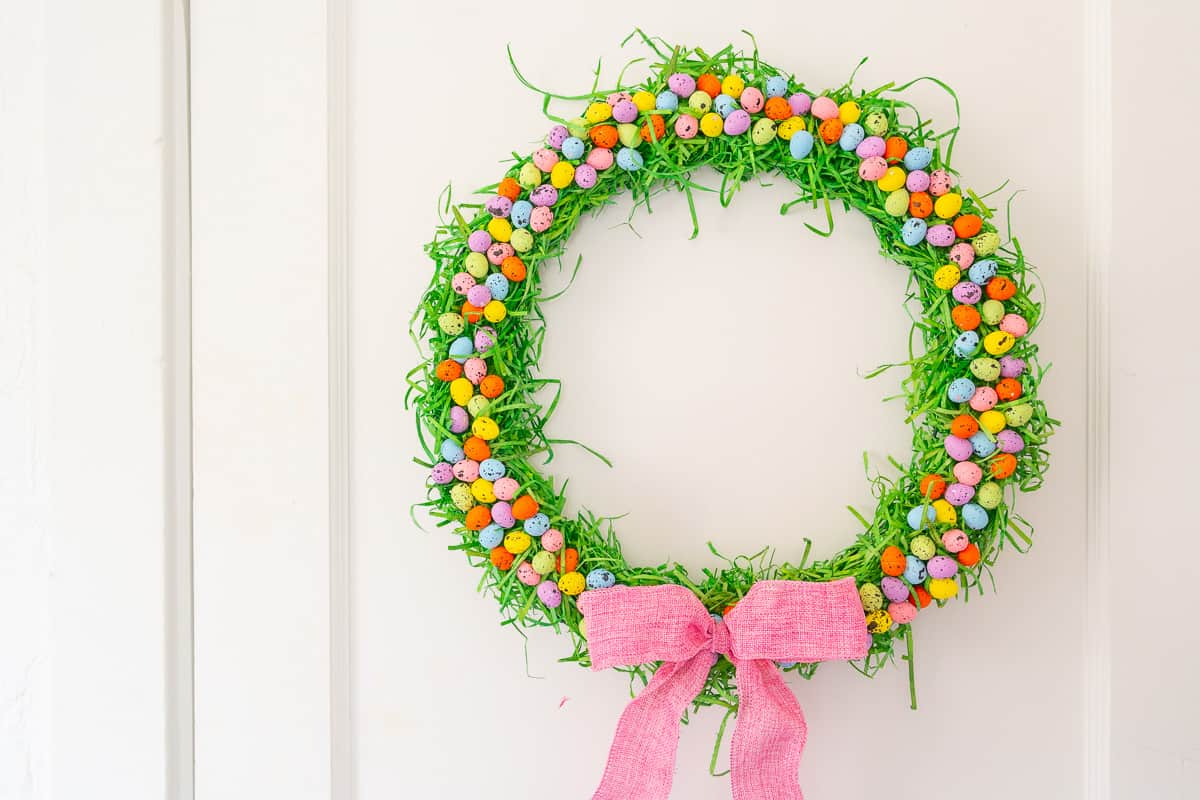 Green grass wreath with mini speckled foam eggs and a pink ribbon.