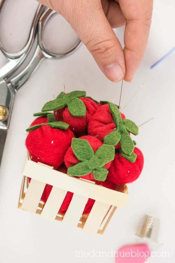 Hand placing needle in a Strawberry Pincushion.