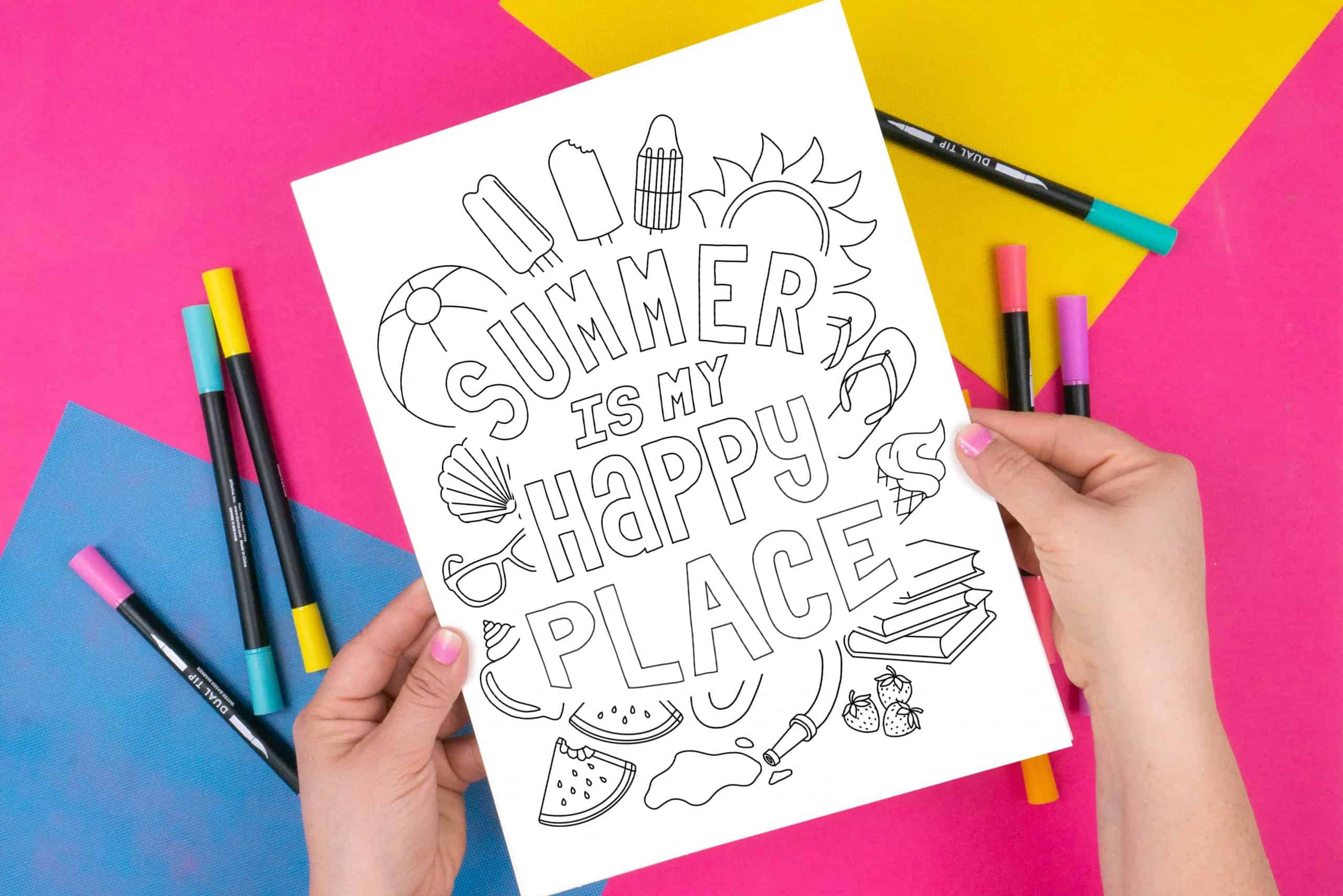 Hands holding Summer Happy Place Free coloring page on a pink background with markers.