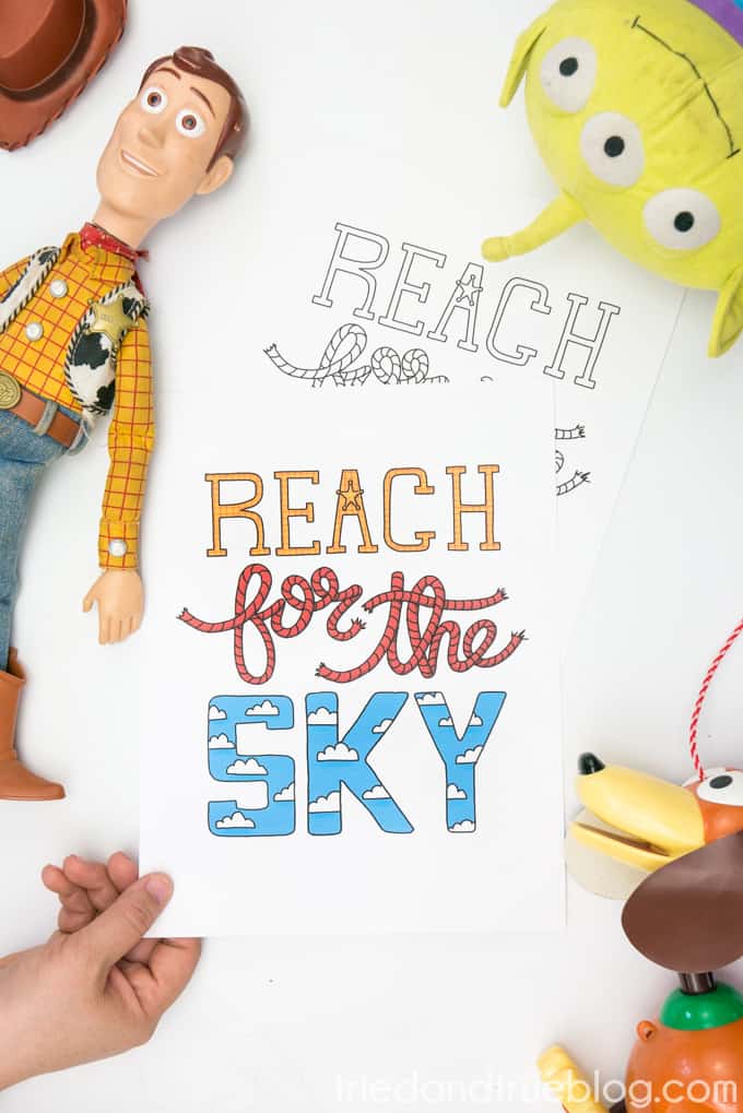 Toys surrounding hand holding Toy Story "Reach for the Sky" free printable.