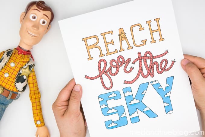 Hands holding color "Reach for the Sky" with Woody doll to the left.