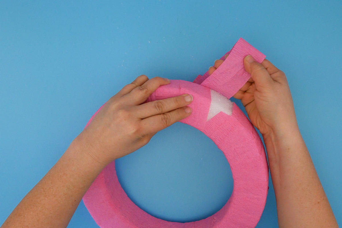Hand wrapping pink crepe paper around foam wreath