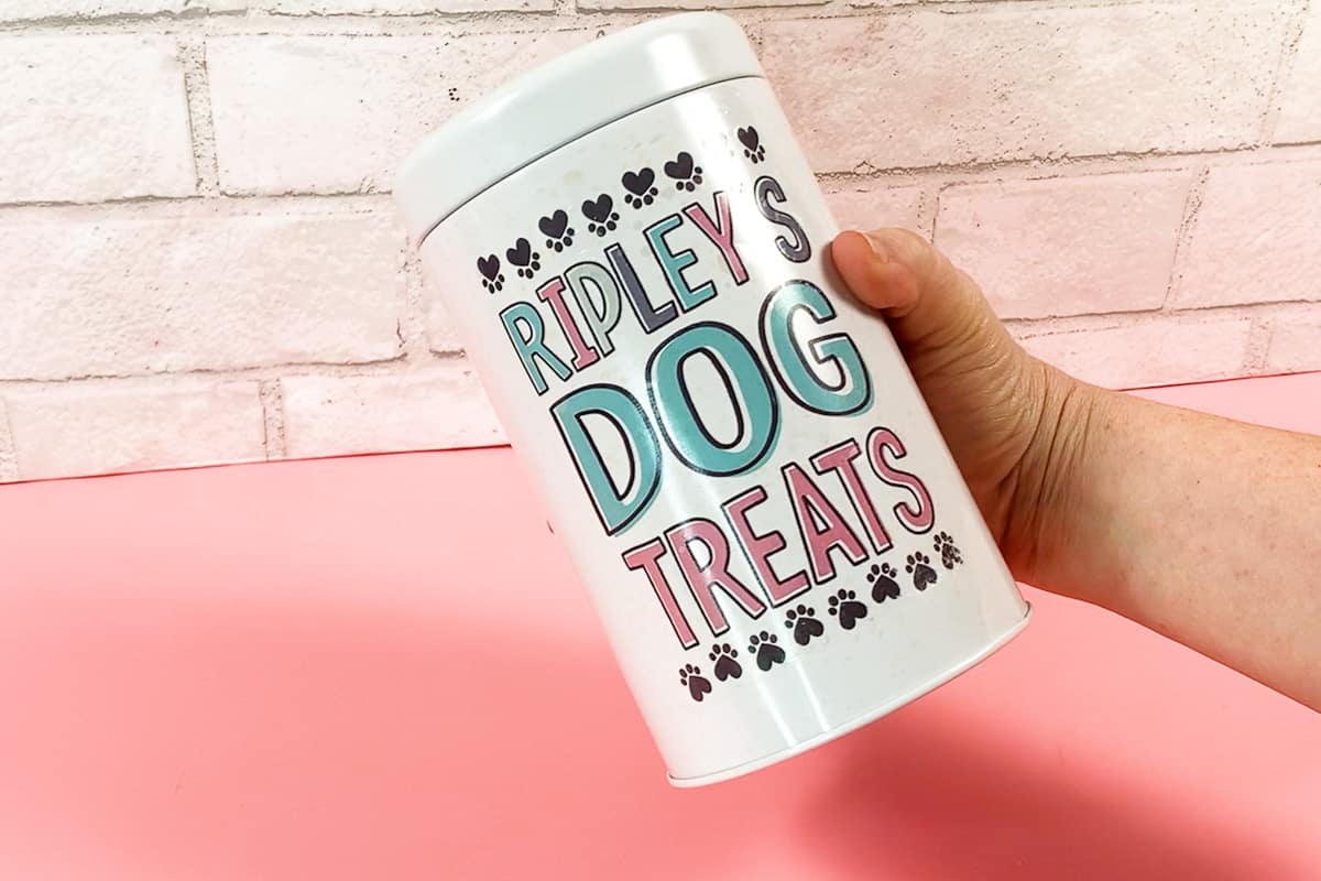 Hand holding a dog treat holder with a waterslide decal that says 