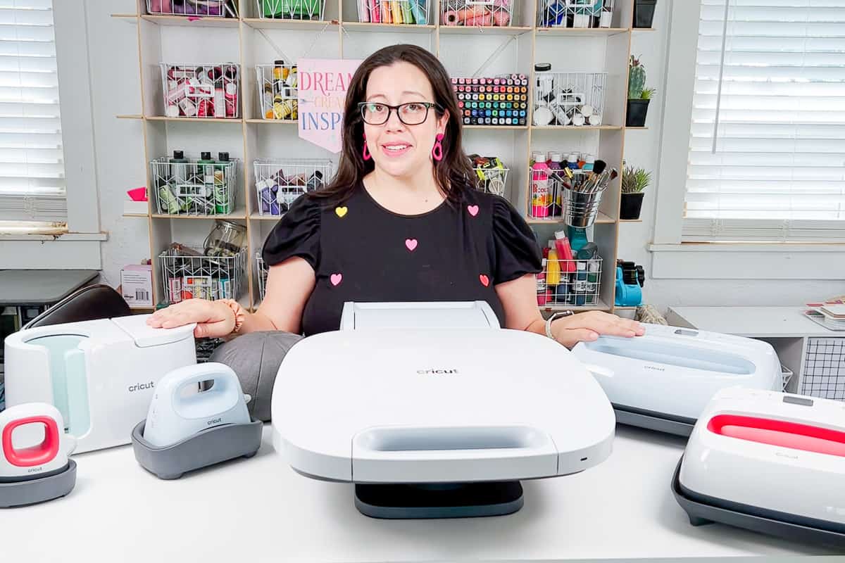Woman in black tshirt with hearts standing behind a variety of Cricut heat presses