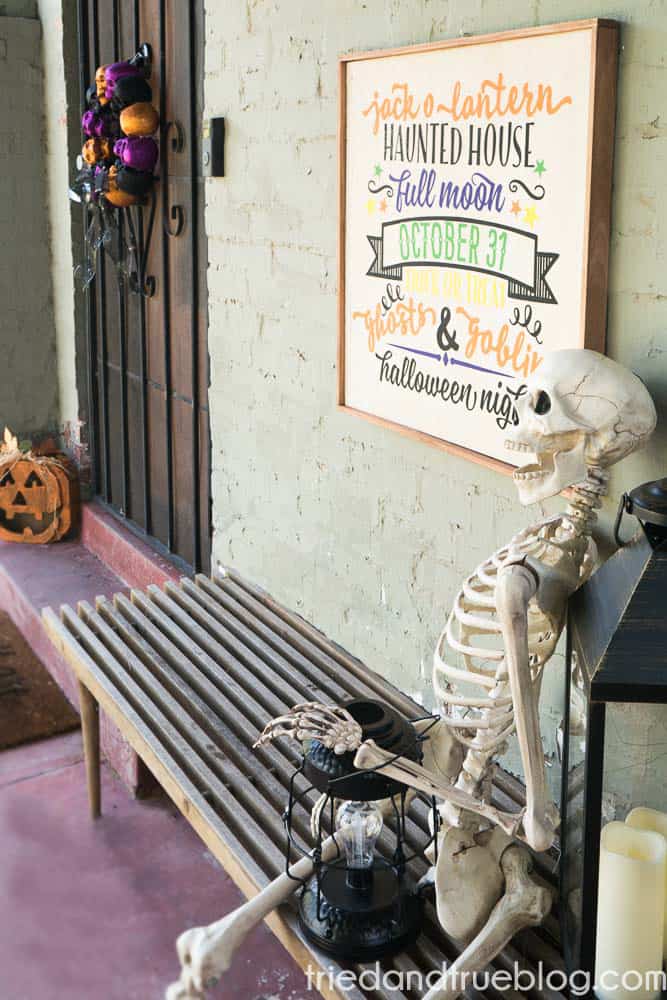 Skeleton sitting on bench in front of Reversible Halloween & Thanksgiving Cricut Vinyl Sign